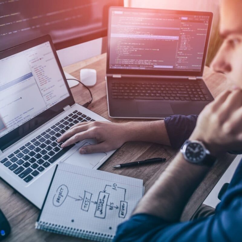 Programmer resting his head on his hand while looking at code on a laptop screen