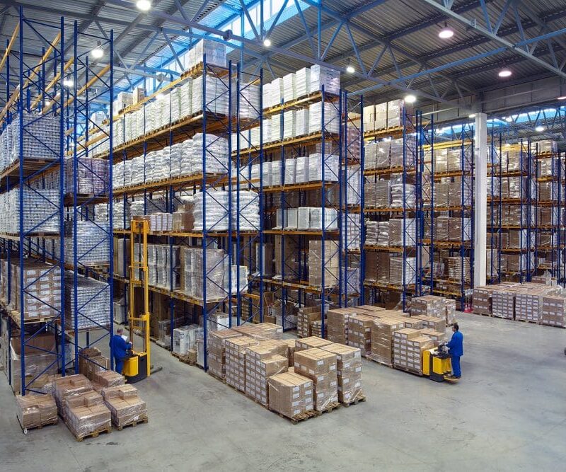 Interior of a large warehouse with tall pallet racking and forklifts moving boxes