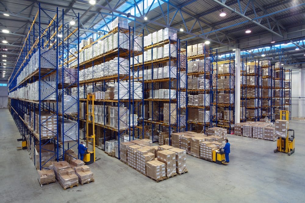 Interior of a large warehouse with tall pallet racking and forklifts moving boxes