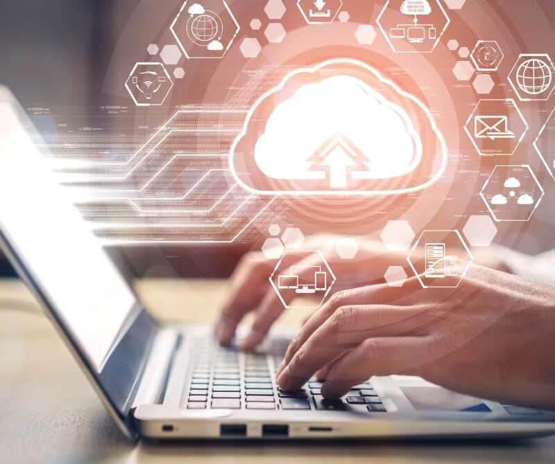 Hands typing on a laptop with a cloud computing icon overlay graphic