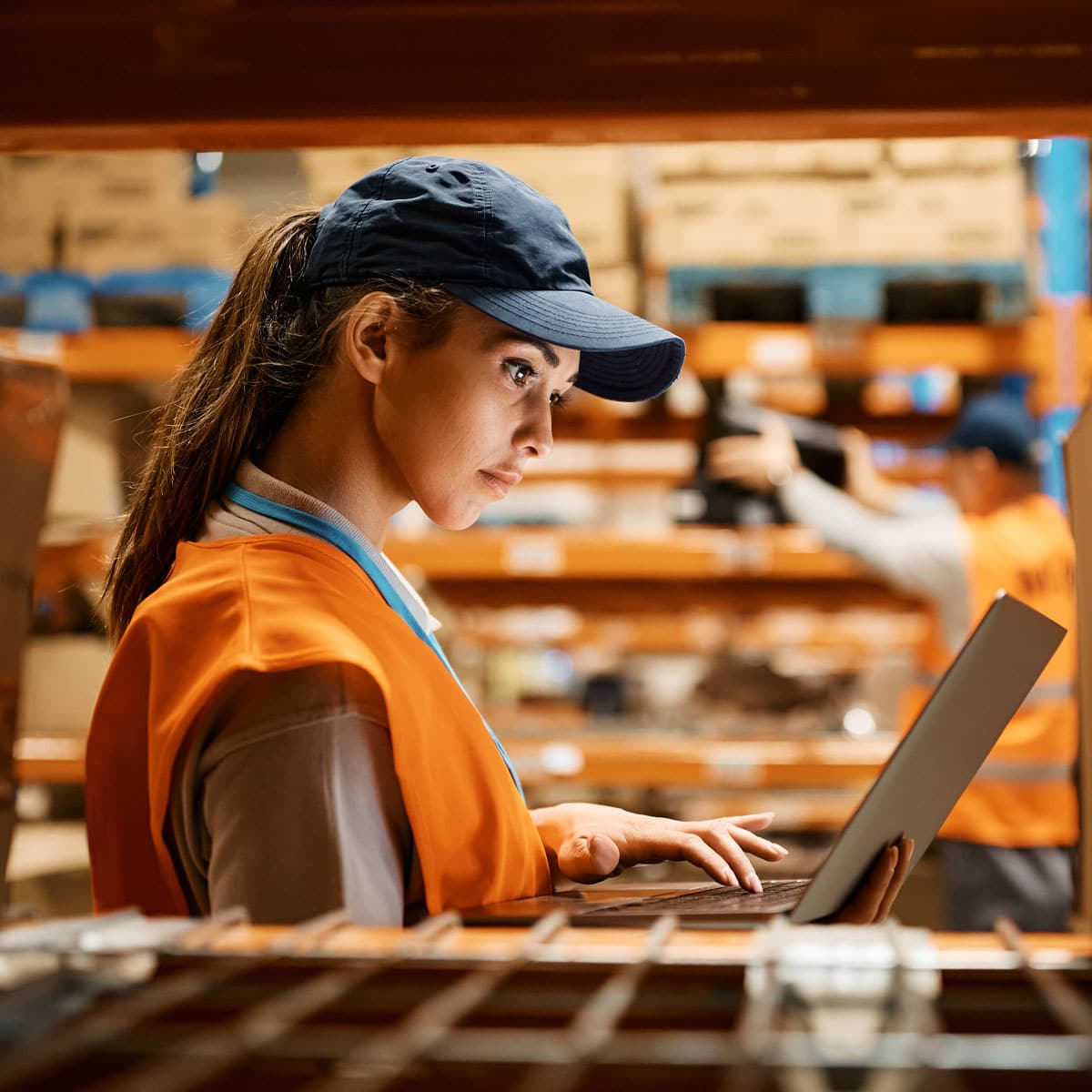 Warehouse worker in a safety vest holding a tablet while looking across the floor