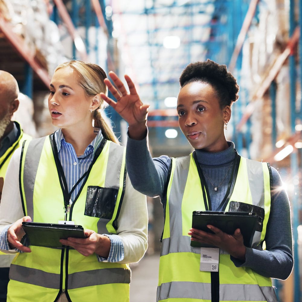 Two warehouse workers in hi-vis vests discussing operations