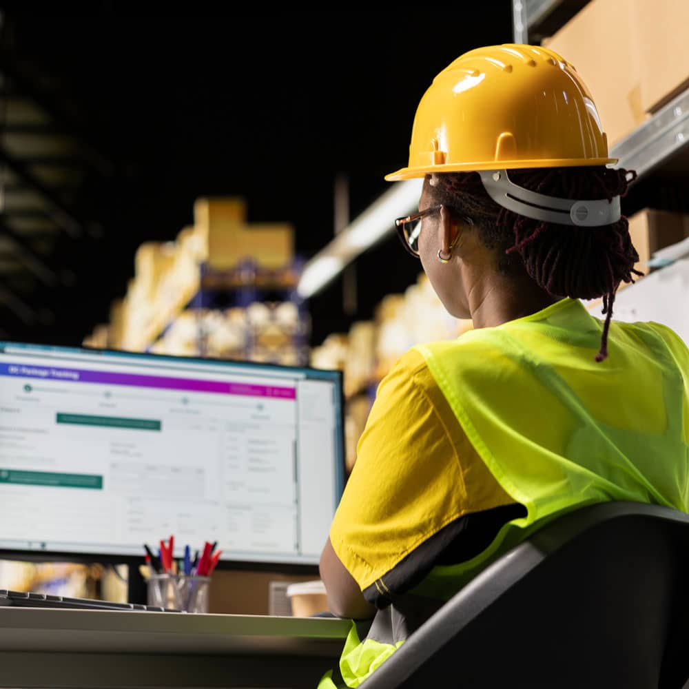 Warehouse worker in a hi-vis vest viewing a software testing dashboard on a screen
