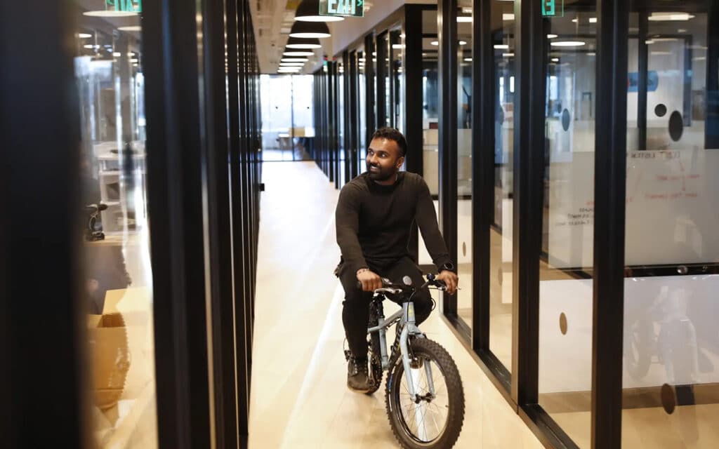 about-slider-3 Man walking a bicycle through a modern glass-walled office hallway
